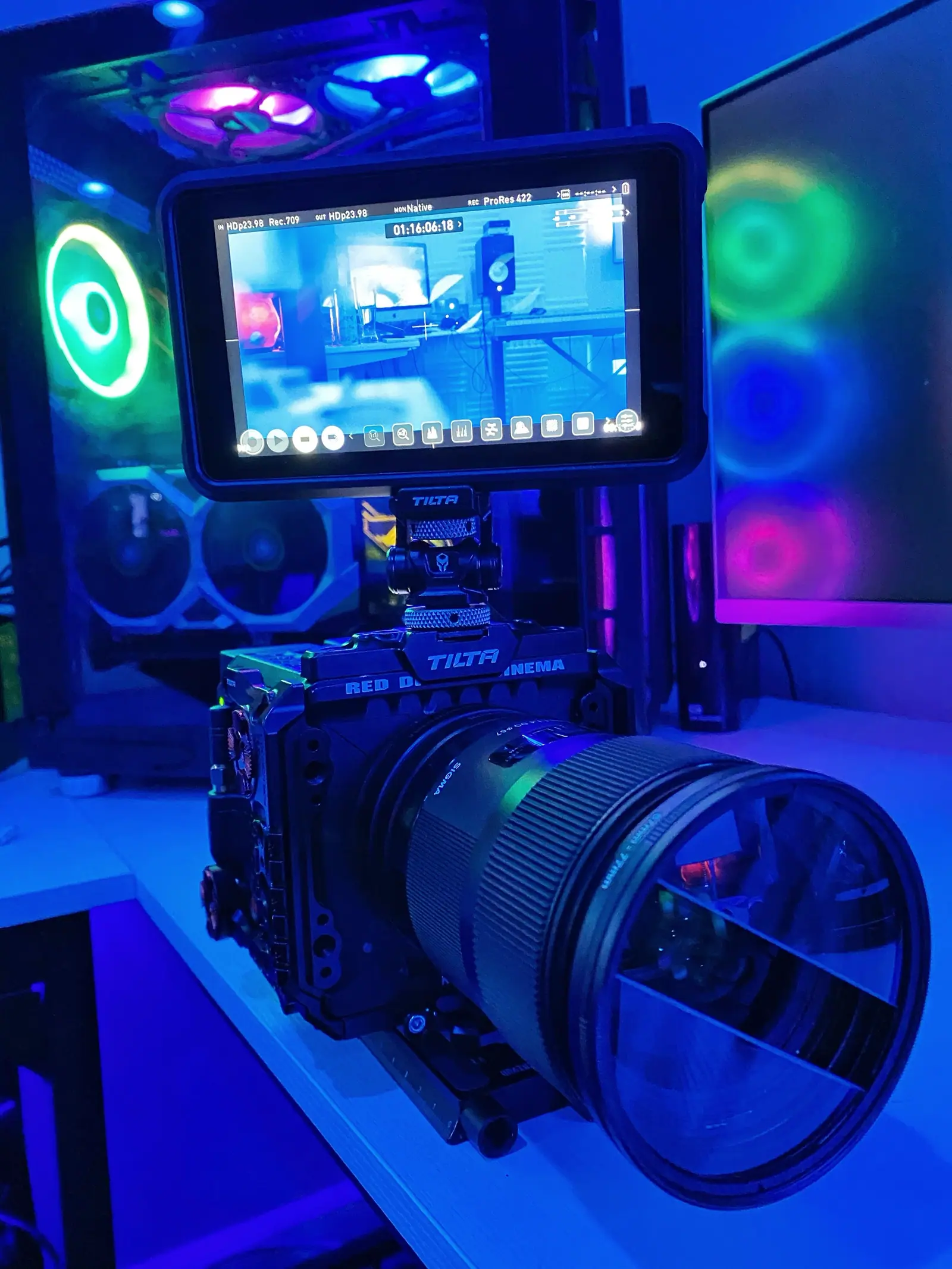 A cinema camera rig in front of an RGB-lit workstation