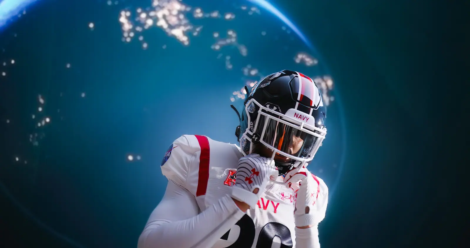 Close on a Navy football player in his helmet, the LED wall glowing blue behind