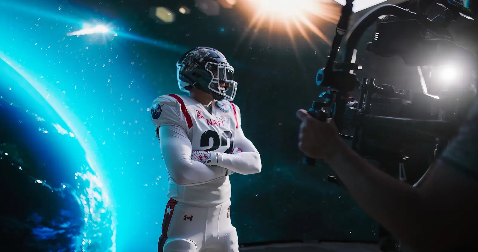 A Navy football player, arms crossed, in front of Earth on the LED wall, Steadicam in frame