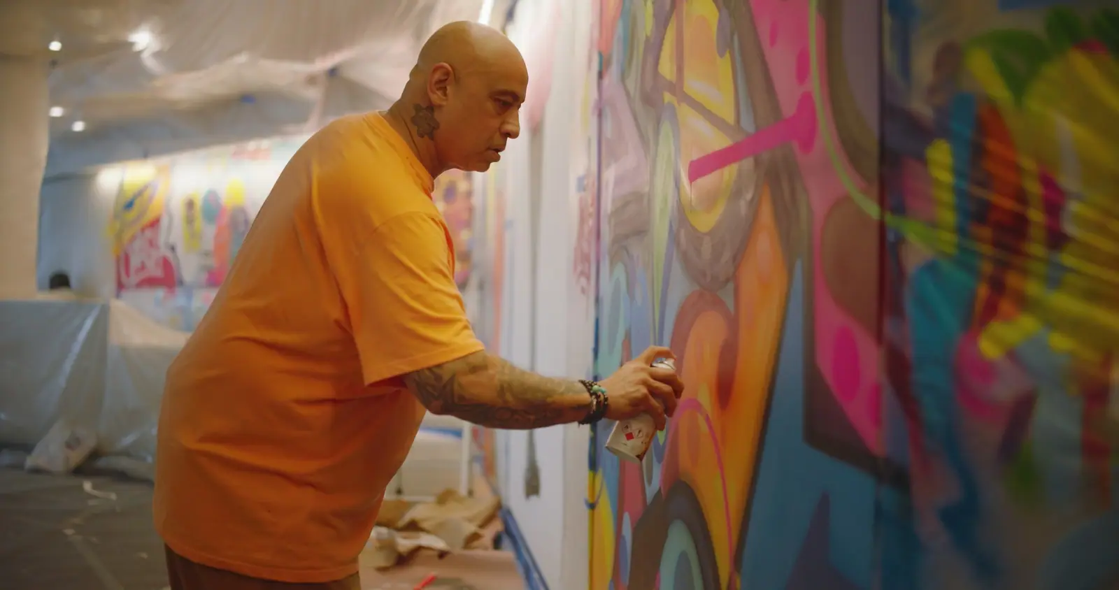 An artist in an orange shirt spraying a panel