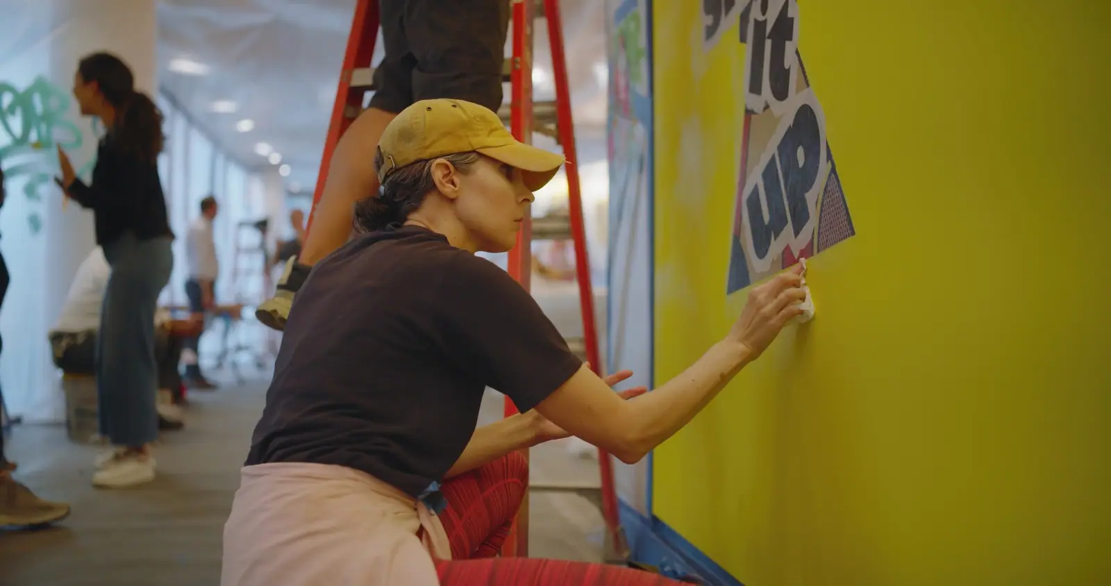 PhoebeNewYork on a ladder, pasting up “shake it up”